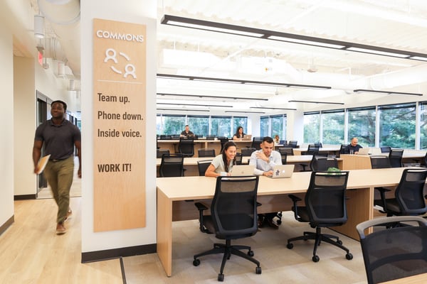 remote work office space with two people looking at laptop and a man walking down hallway